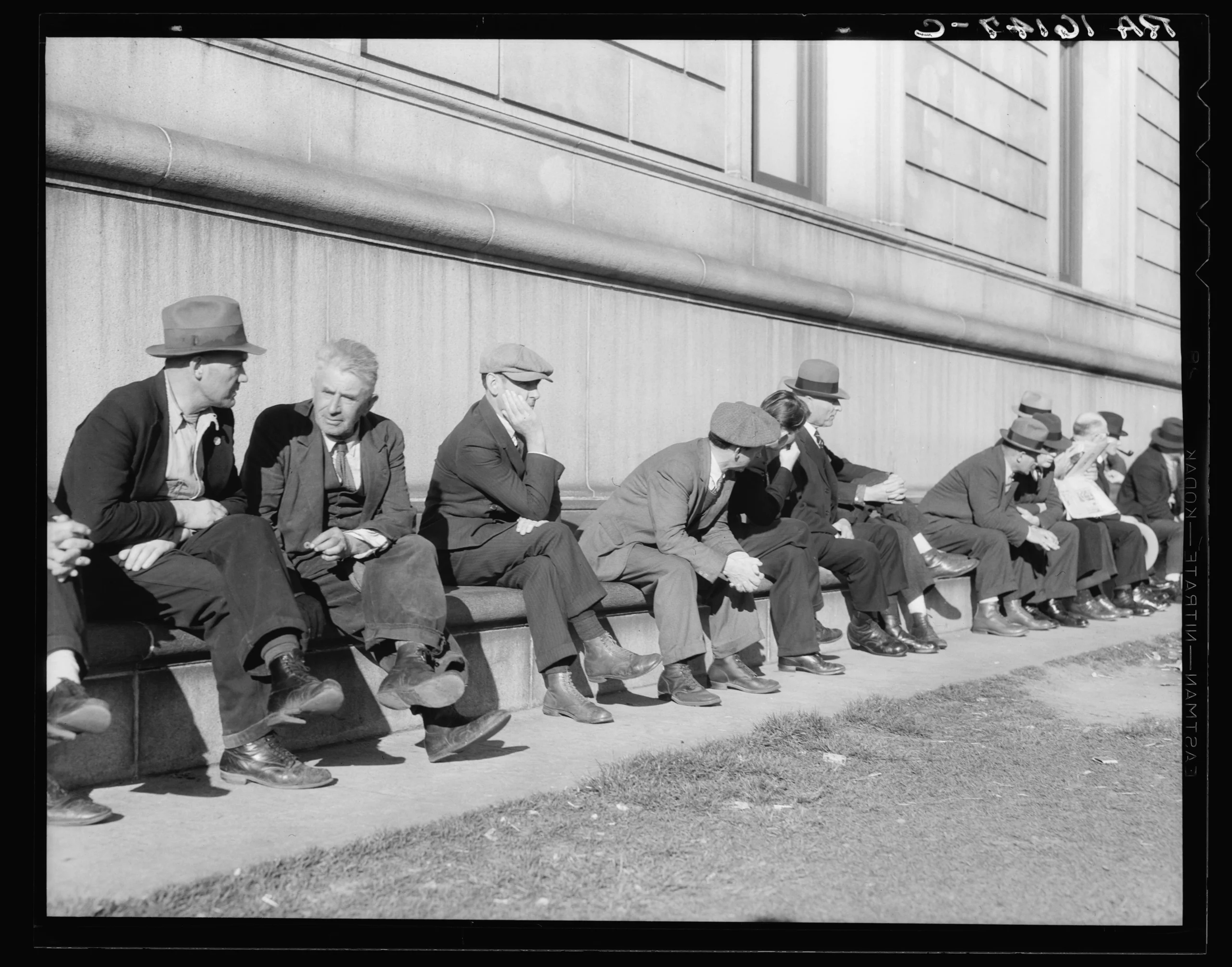 Photograph of unemployed men sitting on the sunny side of the San Francisco Public Library.